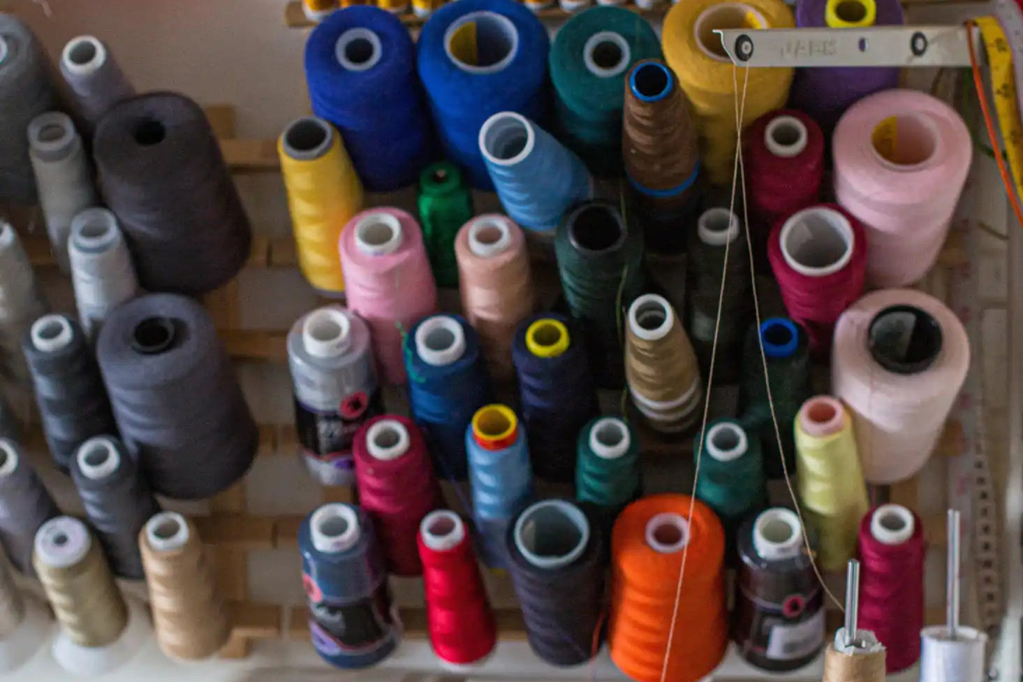 Collection of colorful sewing thread spools arranged on a wall-mounted rack.