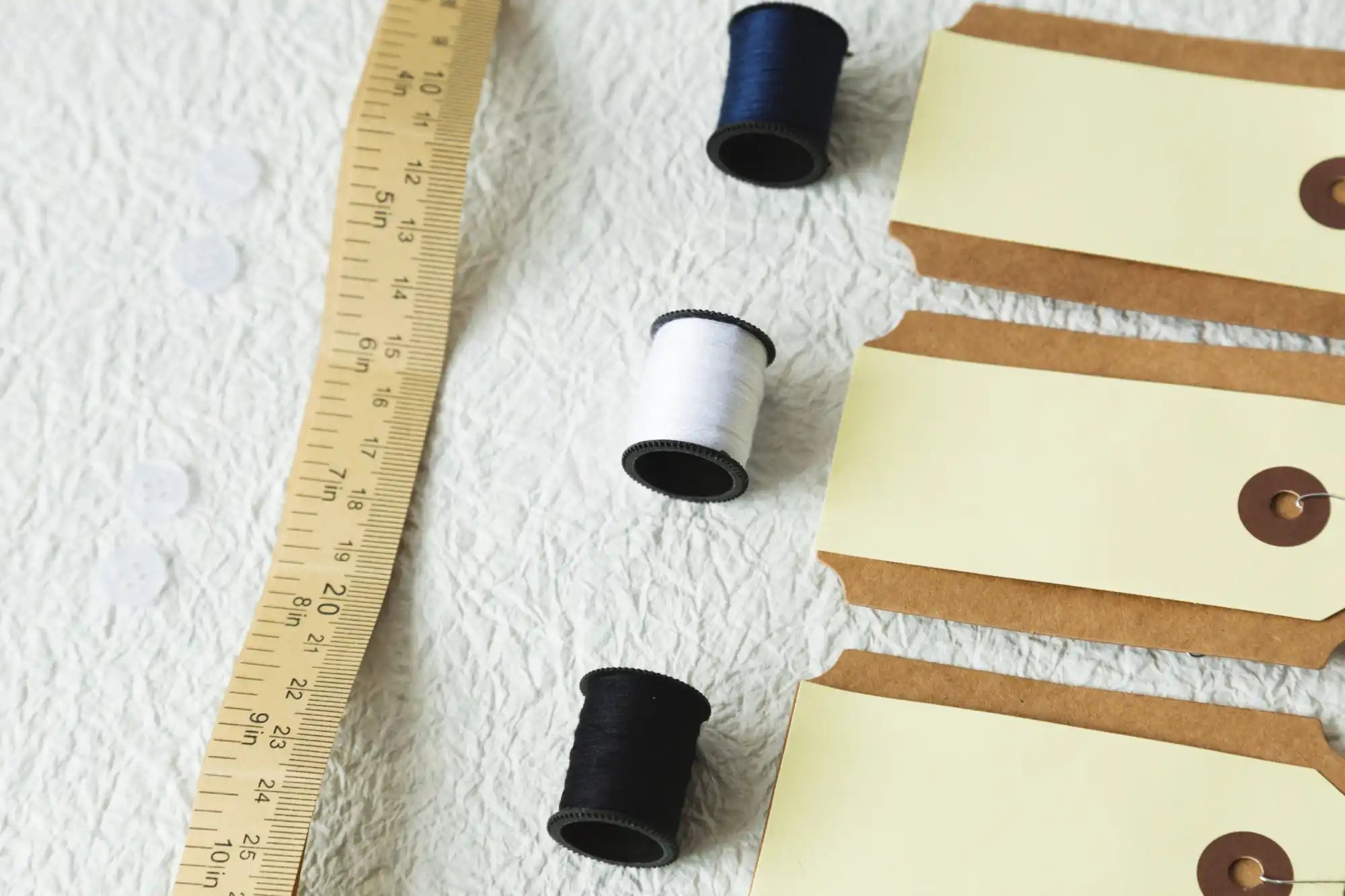 Wooden ruler alongside black and white thread spools and brown paper tags.