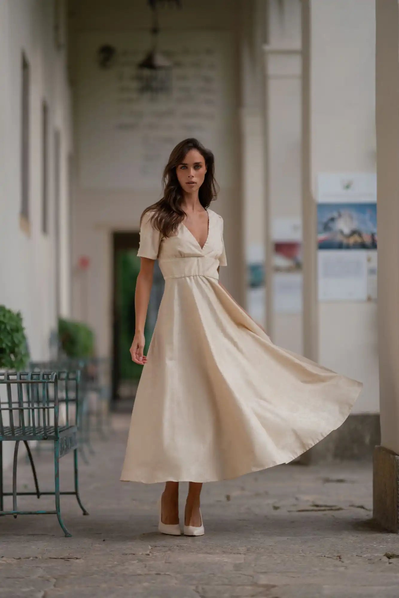 A woman wearing a flowing, short-sleeved, V-neck, cream-colored dress.