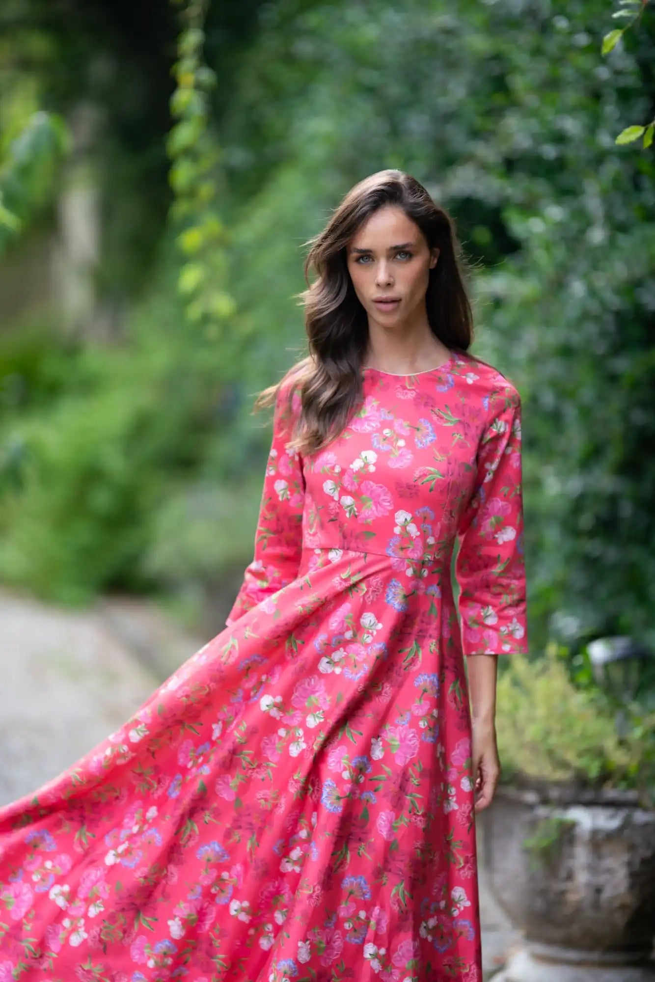 A woman wearing a vibrant, floral-patterned pink maxi dress with three-quarter sleeves.